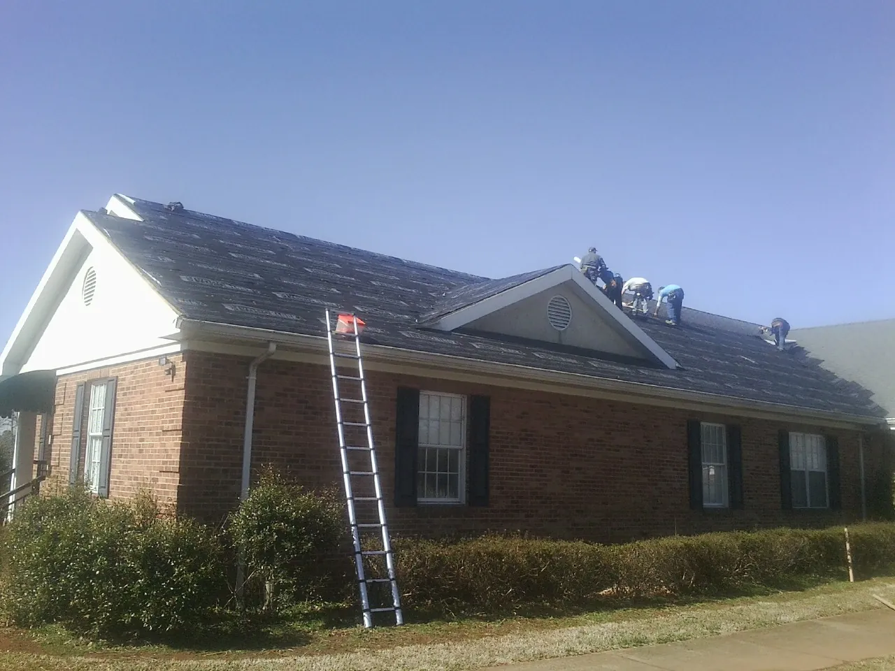 Crew tearing shingles off a brick ranch roof with a ladder set — Metal Roof Repair work by our crew in Newport